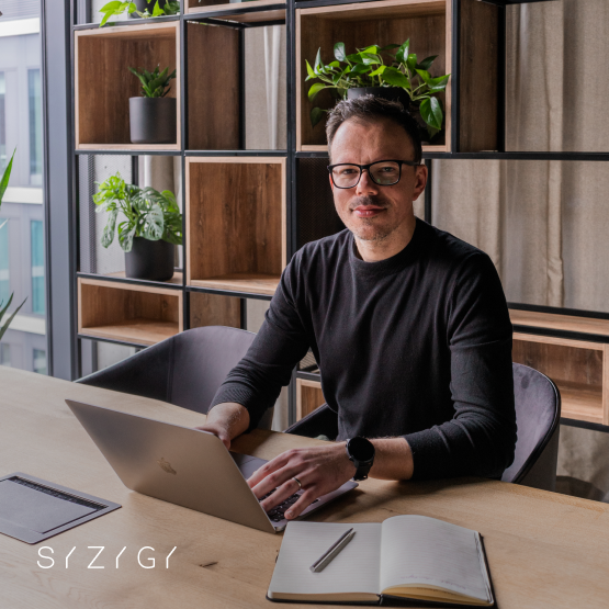 Michał Łukawski, IT Client Partner w SYZYGY Warsaw, ekspert ds. rozwoju produktów cyfrowych i transformacji IT, przy biurku z laptopem, specjalizujący się w doradztwie technologicznym oraz optymalizacji procesów biznesowych.